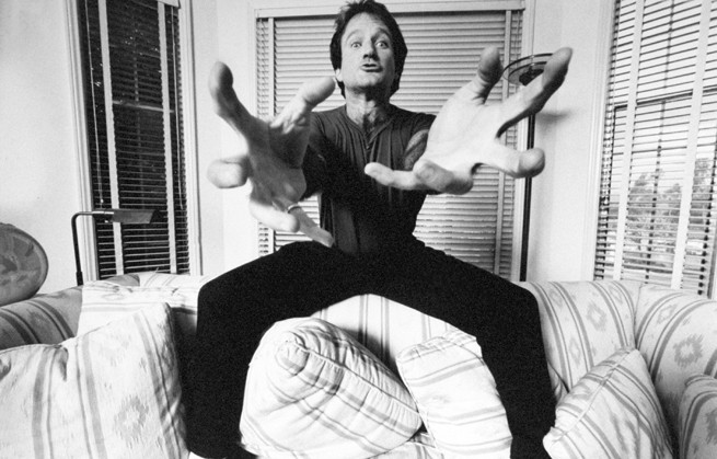 Actor/comedian Robin Williams standing on couch extending his hands at the camera like a crab.